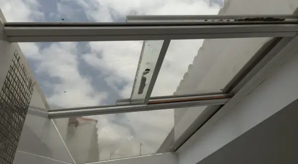 Techos de cristal inconvenientes: suciedad y óxido en los marcos, reflejando un cielo nublado y edificios.