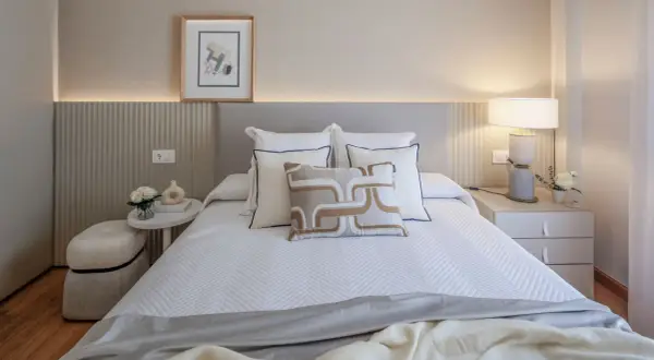 Elegantes ideas de habitaciones de matrimonio con cama blanca, cojines decorativos y mesita de noche con lámpara.