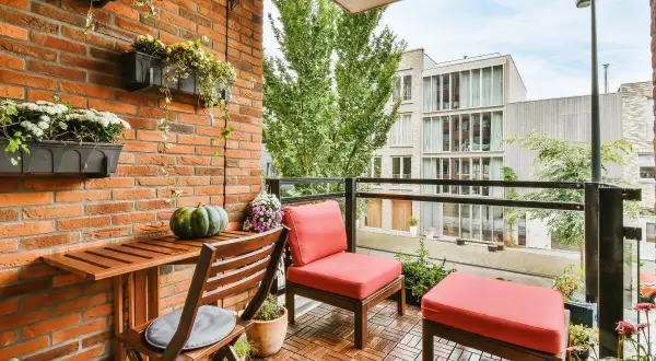 Un balcón alargado decorado con muebles de madera, cojines rojos y plantas colgantes. Un espacio acogedor para disfrutar del exterior.