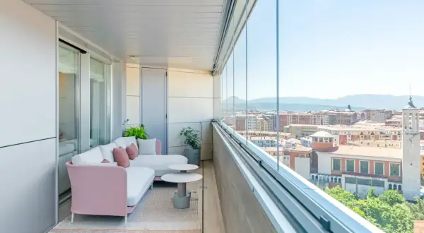 Sofá rosa y blanco en terrazas acristaladas con decoración moderna. Disfruta de la vista urbana desde este espacio acogedor.