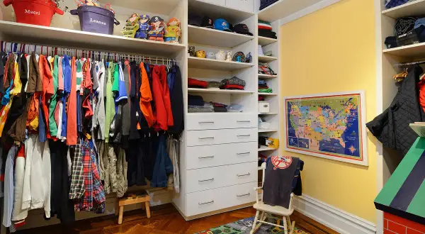 Armario infantil con ropa colgada en la barra, estantes con juguetes y cajones. La altura de la barra del armario es perfecta para los niños.