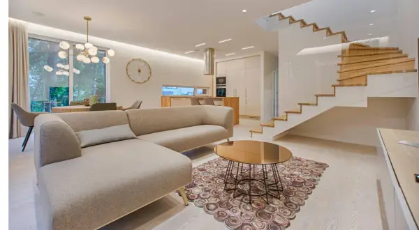 Elegantes ideas de interiores de casas: sofá moderno, mesa de centro dorada, alfombra circular y escaleras de madera flotantes.