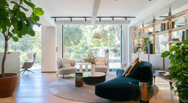 Amplio salón con sofás curvos, sillones, mesas de centro y estanterías, todo bañado por luz natural a través de grandes ventanas modernas.