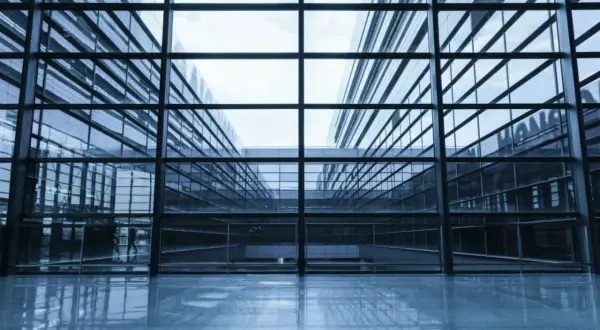 Interior de un edificio moderno con amplios muros cortina de cristal que reflejan el cielo y la arquitectura circundante.