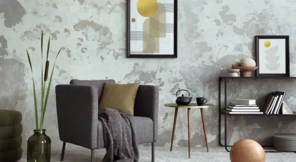 Salón moderno con pared texturizada que combina papel pintado y pintura. Sillón gris, mesa auxiliar dorada y arte abstracto.