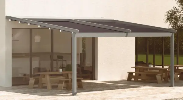 Pérgola moderna con techo oscuro, ideal para saber como cubrir un patio de la lluvia y disfrutar del exterior. Mesas de madera y zona ajardinada.