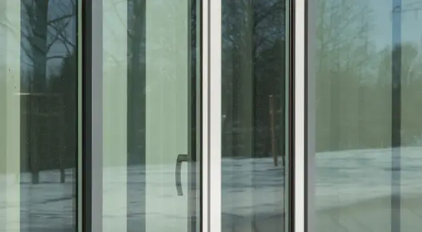Ventana con cristal planitherm, reflejando árboles y nieve. Un tirador plateado se ve en el panel central.