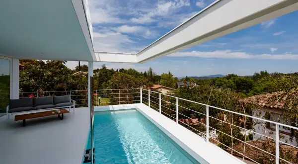 Una moderna piscina en ático con vistas a un paisaje verde. Un sofá gris y una mesa de centro completan el espacio.
