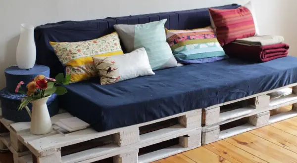 Sofá hecho como hacer un sofa con palets, con cojines coloridos y mantas.