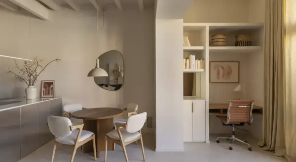 Comedor y zona de trabajo en mini pisos. Mesa redonda, sillas blancas, escritorio con silla de cuero y estanterías.