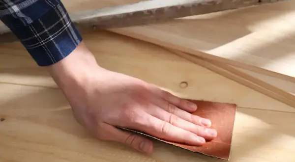 Mano lijando madera con lija, preparando la superficie para un acabado perfecto.