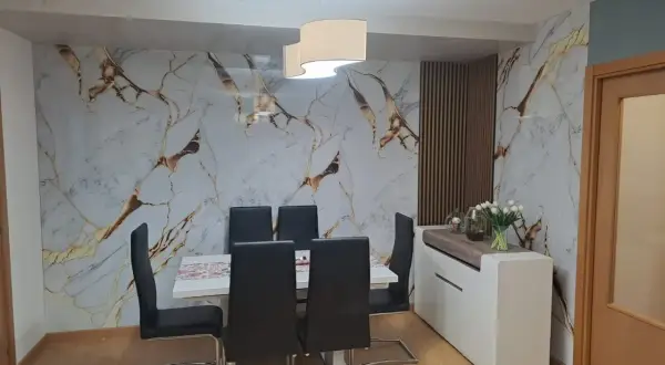 Comedor moderno con pared de mármol y oro, sillas negras y aparador blanco. El cloruro de polivinilo (PVC) es un material versátil.