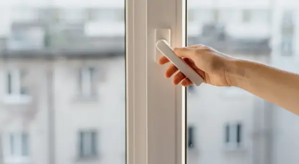 Mano girando la manija de una ventana osciloparalela, quizás para solucionar problemas de apertura o cierre.