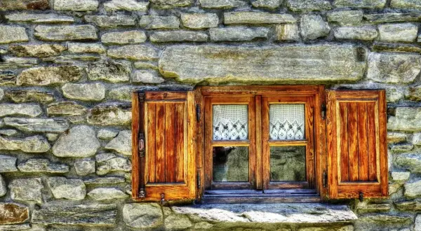 Ventana de madera con contraventanas abiertas, lista para restaurar. Cortinas de encaje blanco adornan los cristales.