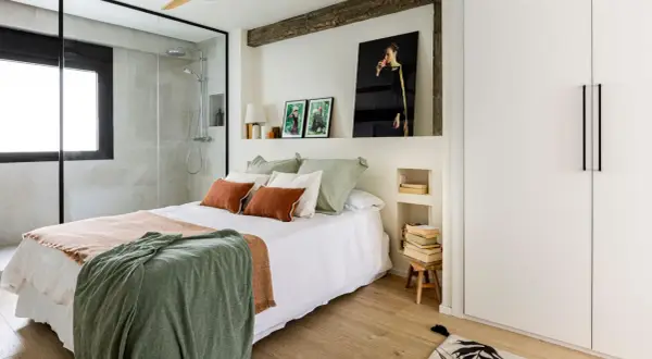 Dormitorio con ducha integrada, cama con mantas cálidas y cuadros. Una reforma sin obras que transforma el espacio con estilo y funcionalidad.