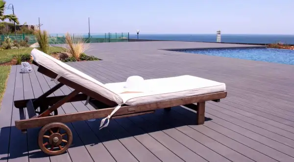 Tumbona lista para el sol sobre una terraza de madera composite, con piscina y mar al fondo.
