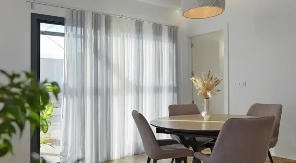 Comedor moderno con mesa y sillas, y diferentes tipos de cortinas que filtran la luz.
