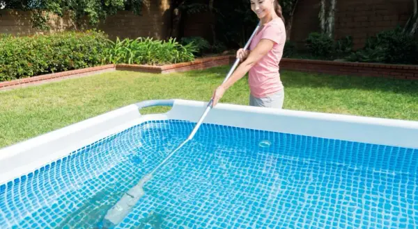 Mujer sonriente realizando el mantenimiento de piscinas con un limpiafondos.