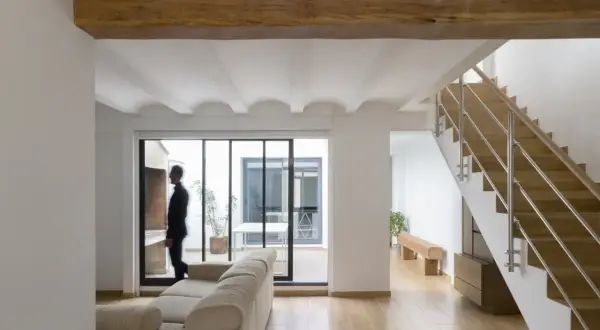 Interior moderno con vigas de madera, escaleras y un hombre mirando al patio. Estimación del precio construir casa 30 m2.
