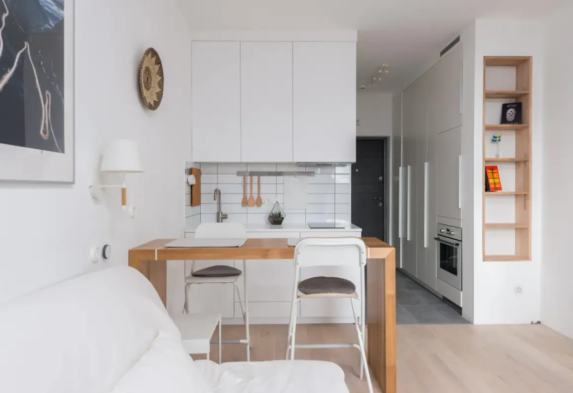 Interiores de casas sencillas con cocina blanca, barra de madera y sofá blanco. Estilo minimalista y funcional.