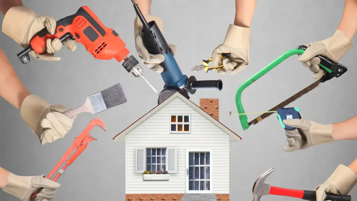 Manos con guantes sostienen herramientas de construcción alrededor de una casa. ¡Calcula tu reforma casa precio!