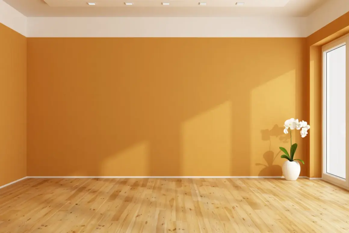 Habitación vacía con paredes de colores cálidos, suelo de madera y una orquídea blanca en una maceta.