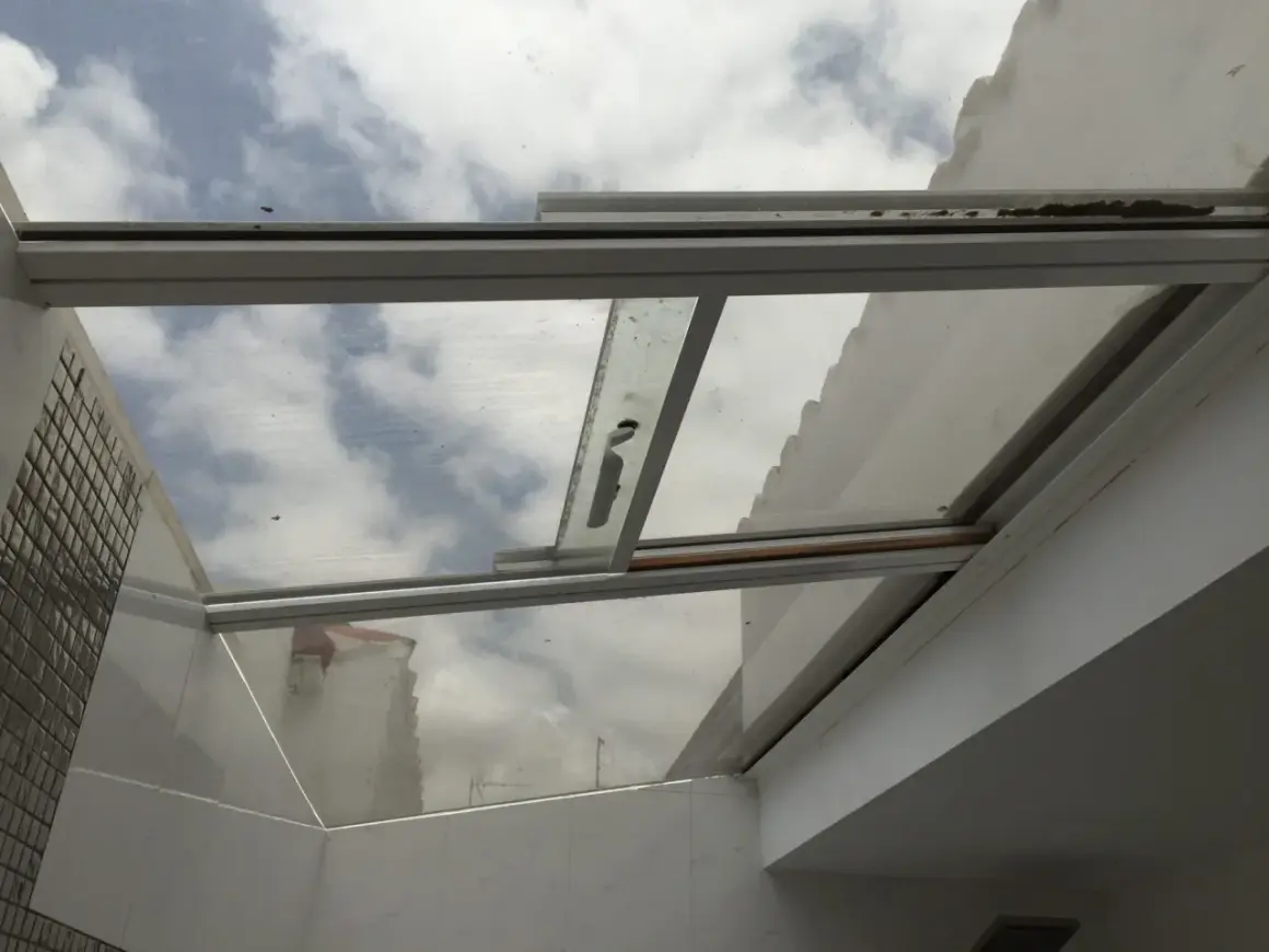 Techos de cristal inconvenientes: suciedad y óxido en los marcos, reflejando un cielo nublado y edificios.
