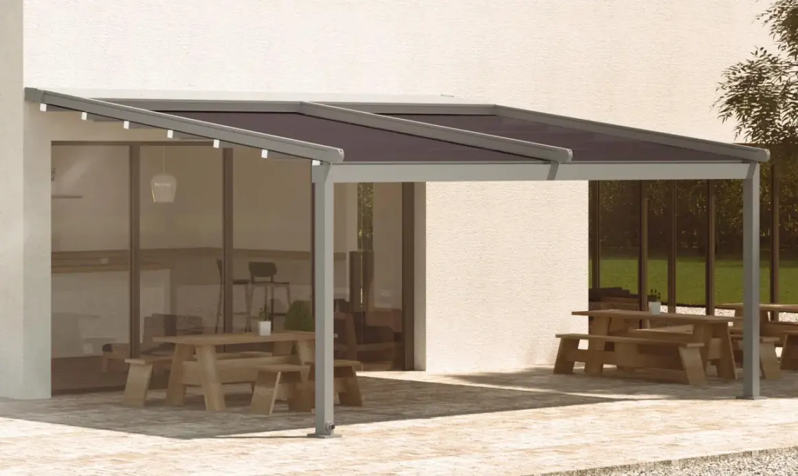 Pérgola moderna con techo oscuro, ideal para saber como cubrir un patio de la lluvia y disfrutar del exterior. Mesas de madera y zona ajardinada.