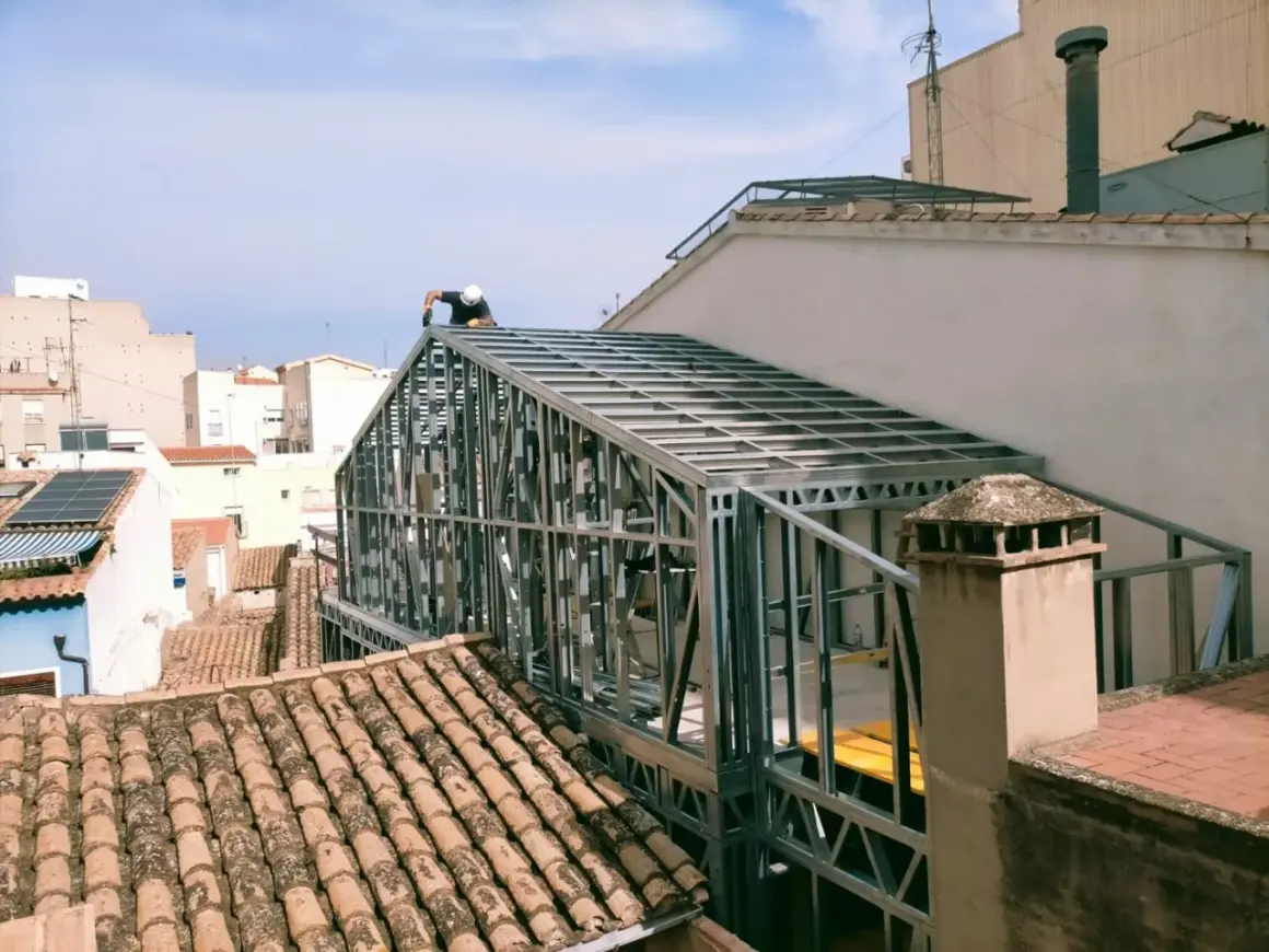 Un trabajador instala un tejado de steel framing sobre un edificio.