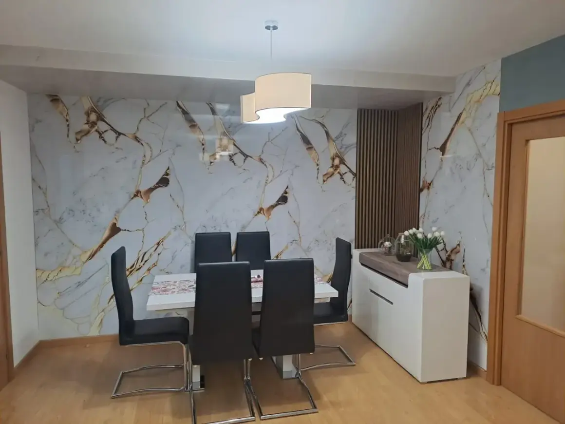 Comedor moderno con pared de mármol y oro, sillas negras y aparador blanco. El cloruro de polivinilo (PVC) es un material versátil.