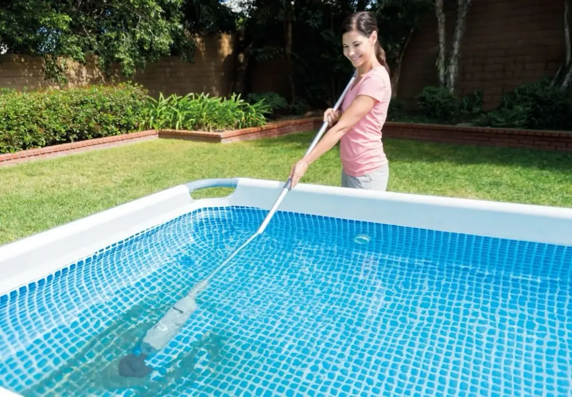 Mujer sonriente realizando el mantenimiento de piscinas con un limpiafondos.
