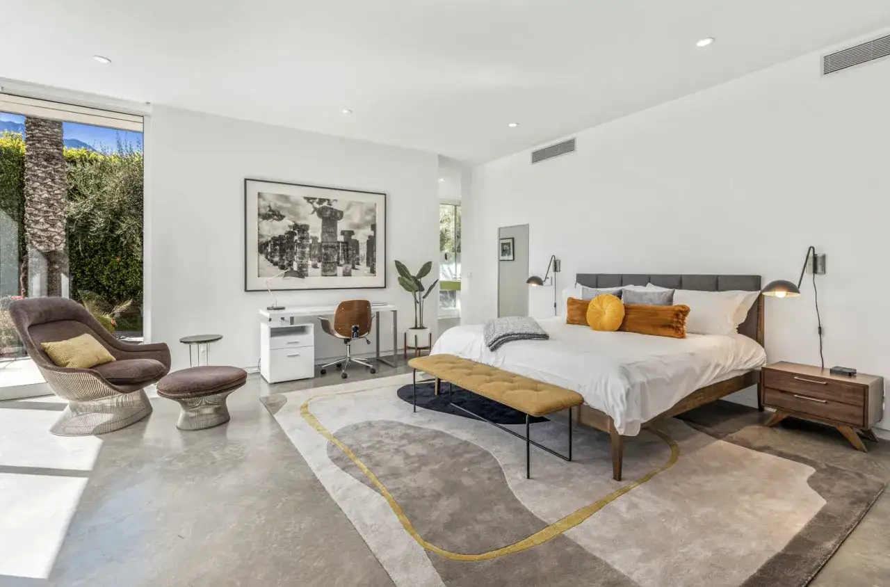 Amplia habitaci&oacute;n con cama de matrimonio, escritorio, sill&oacute;n y alfombra moderna.