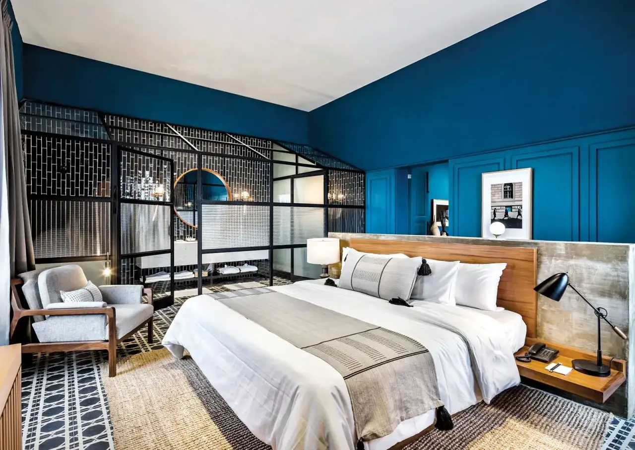 Modernas ideas de habitaciones de matrimonio: cama king, sill&oacute;n gris, ba&ntilde;o abierto con espejo redondo y azulejos negros.
