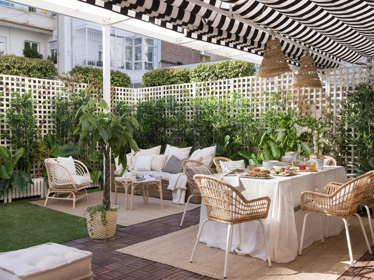 Un rincón de intimidad en la terraza de un ático, con mobiliario de ratán y una mesa puesta para disfrutar.