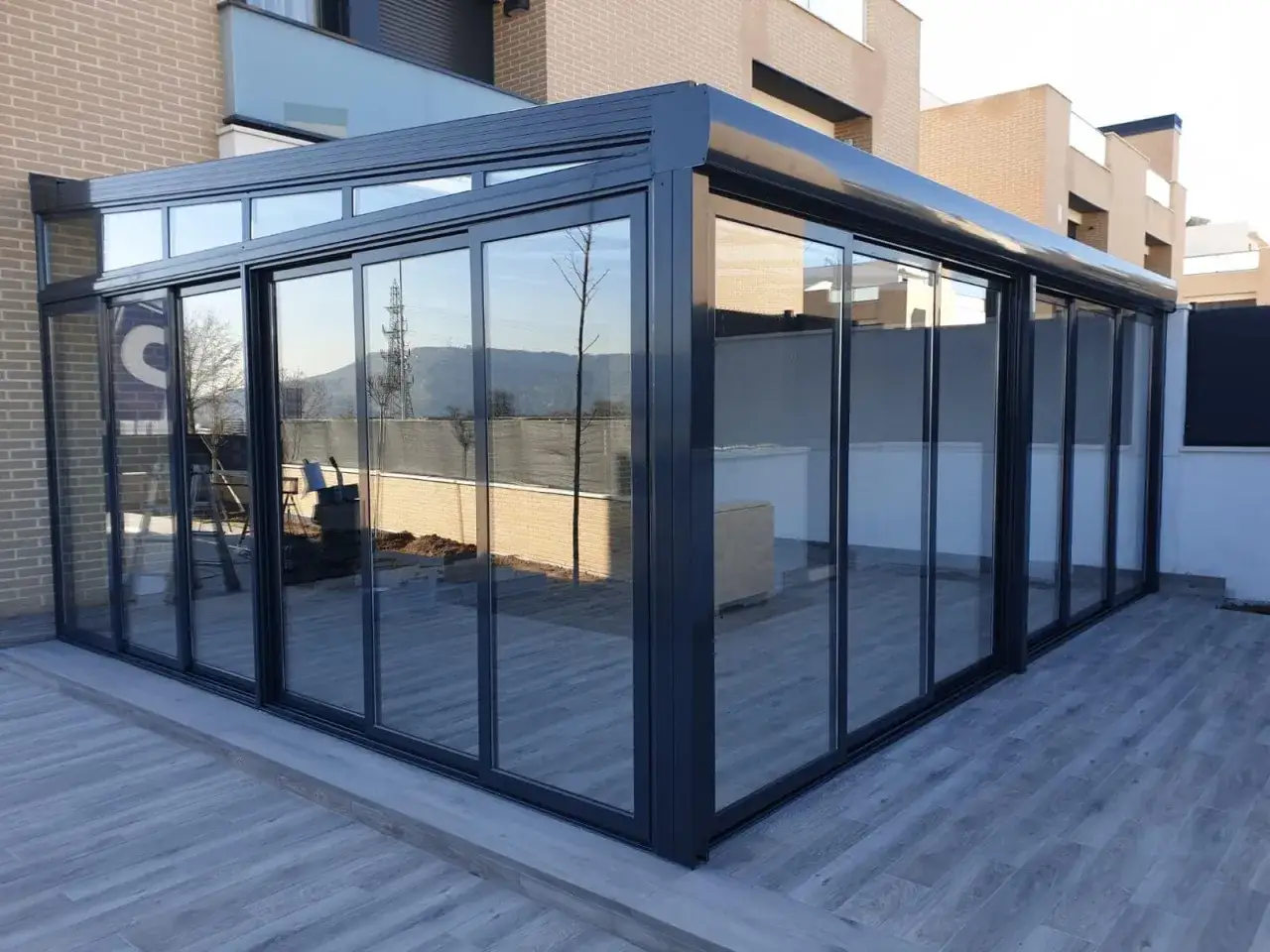 Modernos tipos de cerramientos de cristal con marcos oscuros, creando un espacio luminoso y elegante en una terraza.