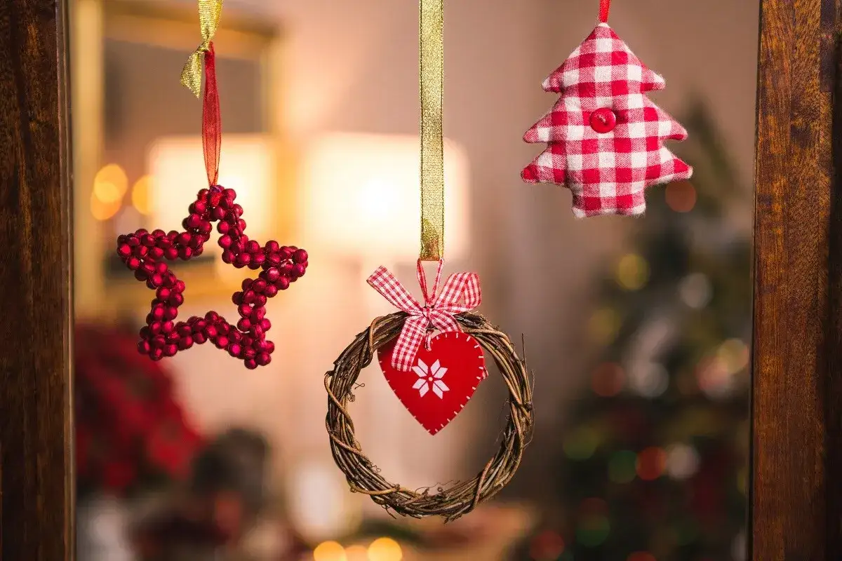 Adornos navideños: estrella roja, corazón en corona de ramas y árbol a cuadros. Ideas para decorar una ventana de navidad.