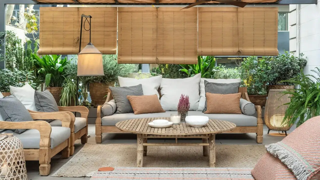 Acogedor salón exterior con sofá, sillones de madera, mesa de centro y muchas plantas. Un rincón perfecto para disfrutar de terrazas pequeñas con encanto.