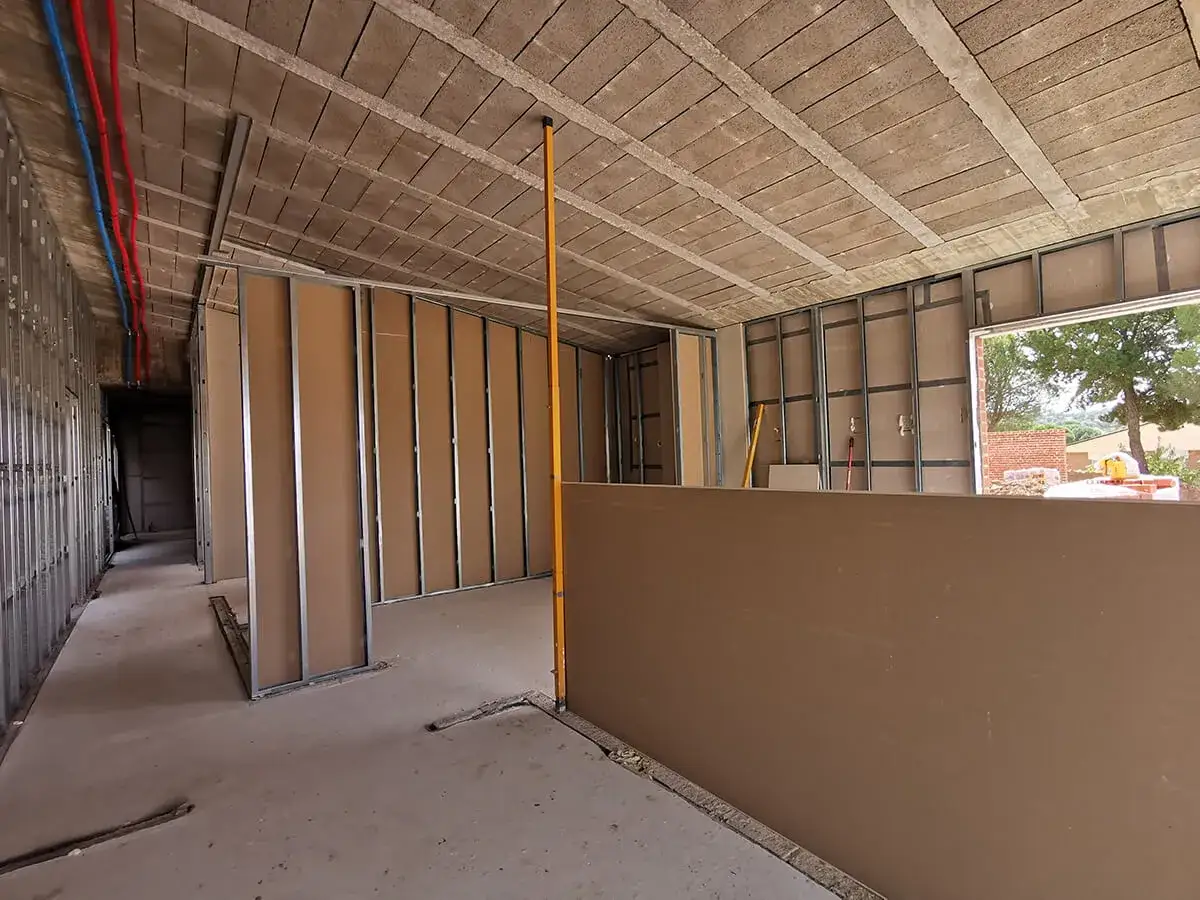Interior de una casa en construcción, con estructuras metálicas y tabiques de cartón yeso. Se aprecian tuberías de agua y el techo de viguetas.