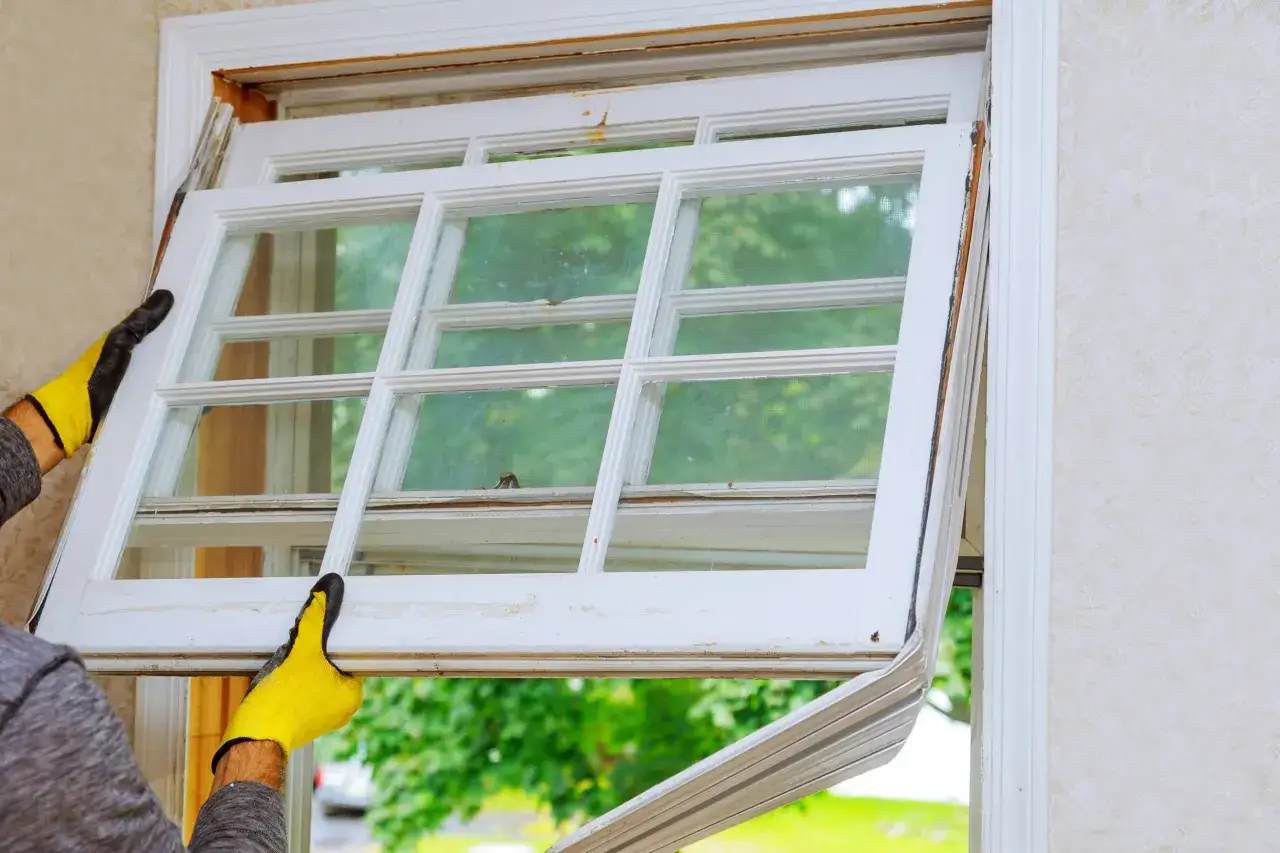 Man con guantes amarillos retirando un cristal de ventana de aluminio para cambiarlo.