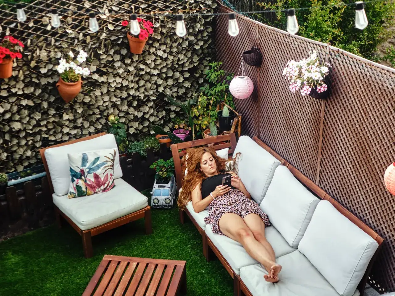 Mujer relajada en un sof&aacute; de patio con c&eacute;sped artificial y luces decorativas. Una soluci&oacute;n para techar patio econ&oacute;mico y acogedor.