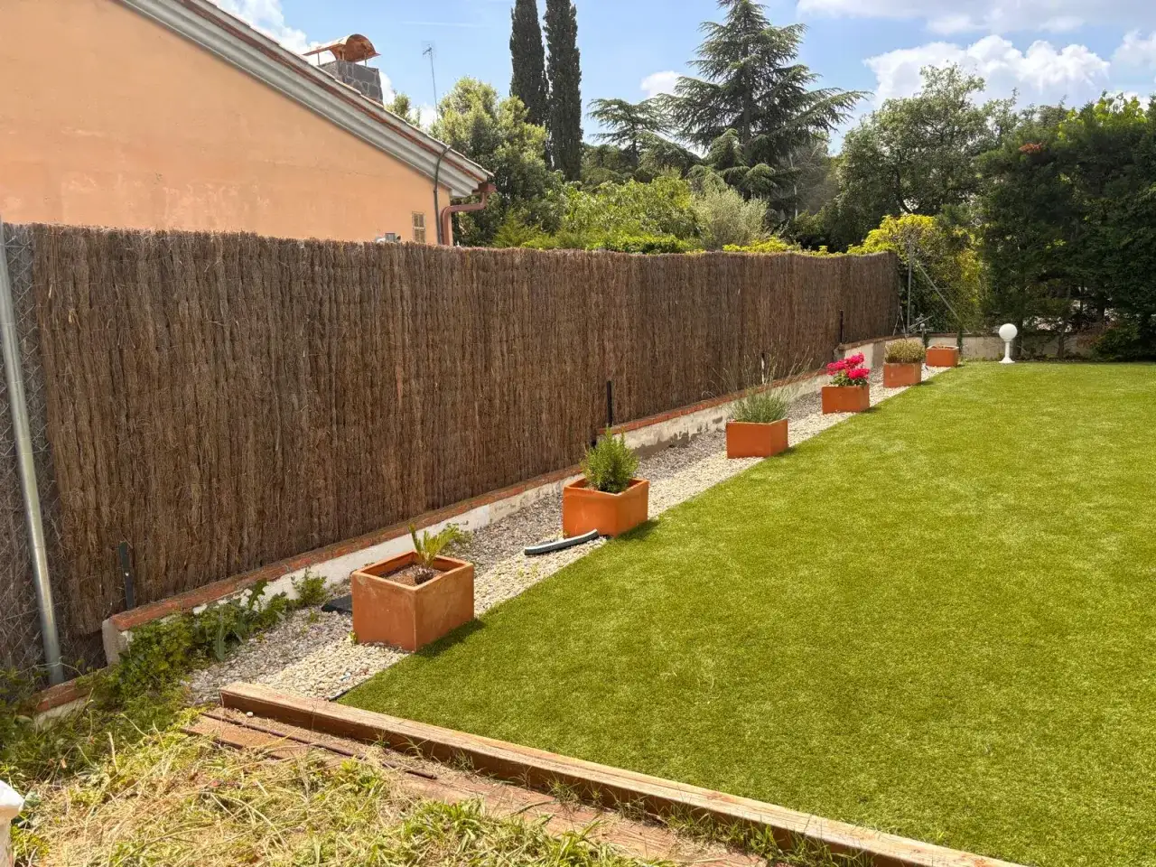 Ideas ocultaci&oacute;n jard&iacute;n: valla de ca&ntilde;izo, c&eacute;sped artificial y macetas con plantas crean un espacio privado y acogedor.