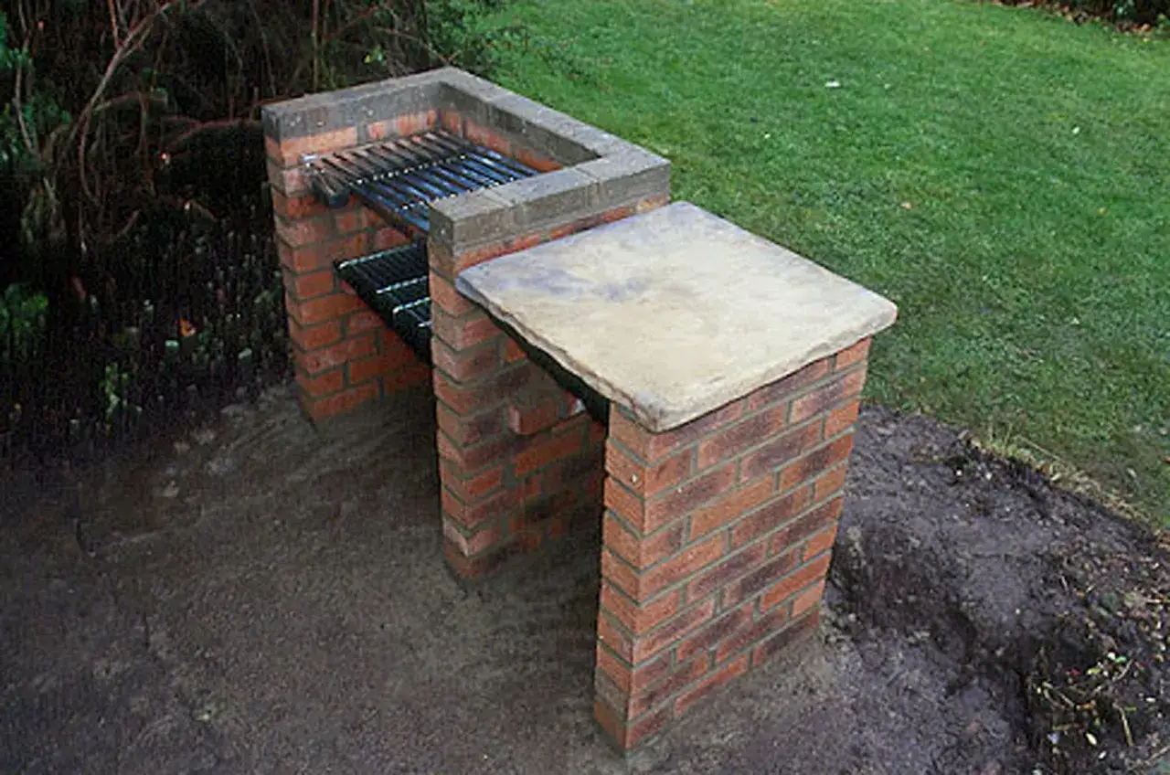 Barbacoa de ladrillo con parrilla y encimera de piedra, lista para hacer barbacoas en el jard&iacute;n.