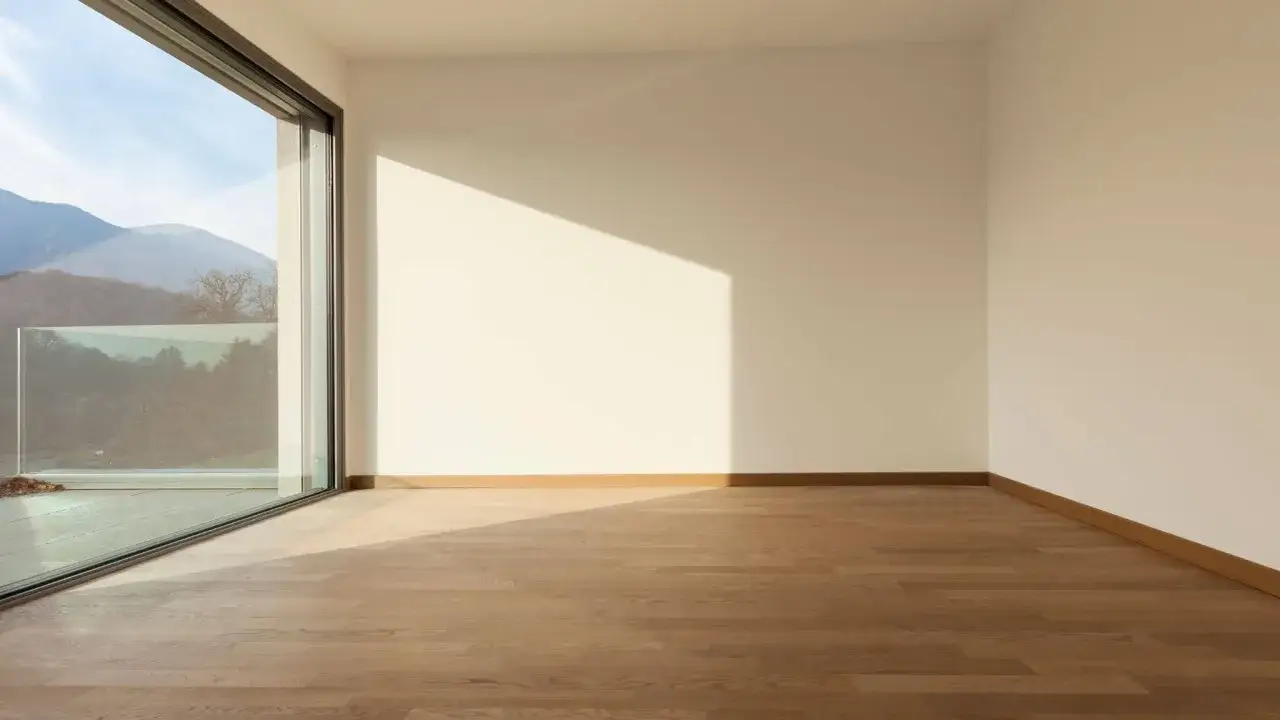 Habitaci&oacute;n vac&iacute;a con suelo de madera y gran ventanal de cristal planitherm que ofrece vistas a monta&ntilde;as.