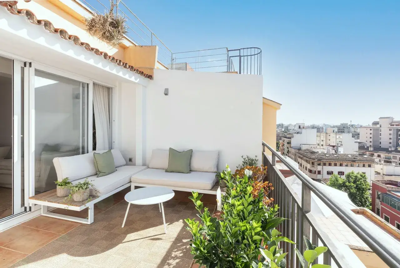 Ideas para decorar un &aacute;tico: terraza con sof&aacute;s blancos, mesa auxiliar y plantas, con vistas a la ciudad.