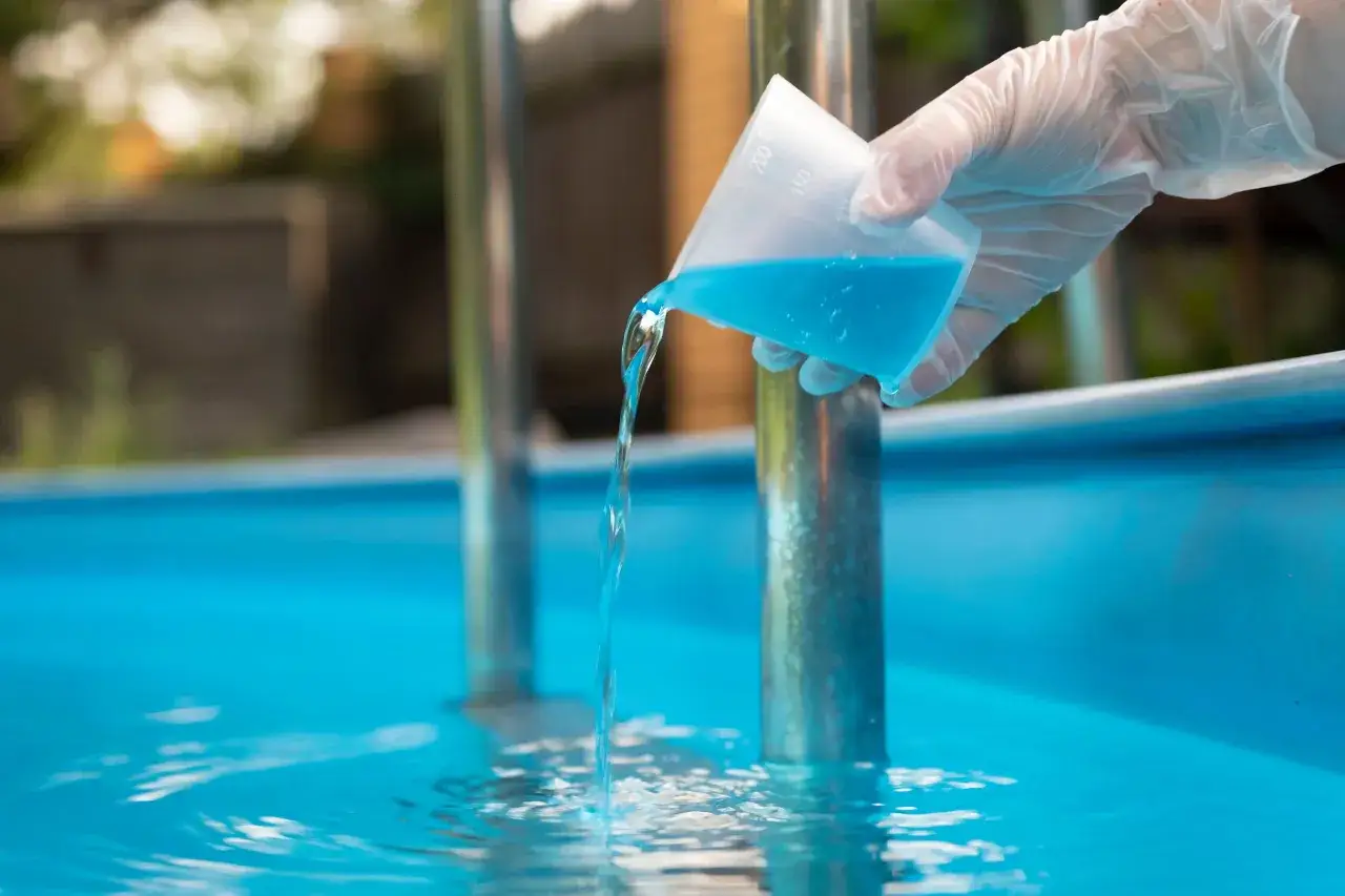 Mano con guante vierte l&iacute;quido azul en piscina. Es parte del mantenimiento de piscinas para mantener el agua cristalina.