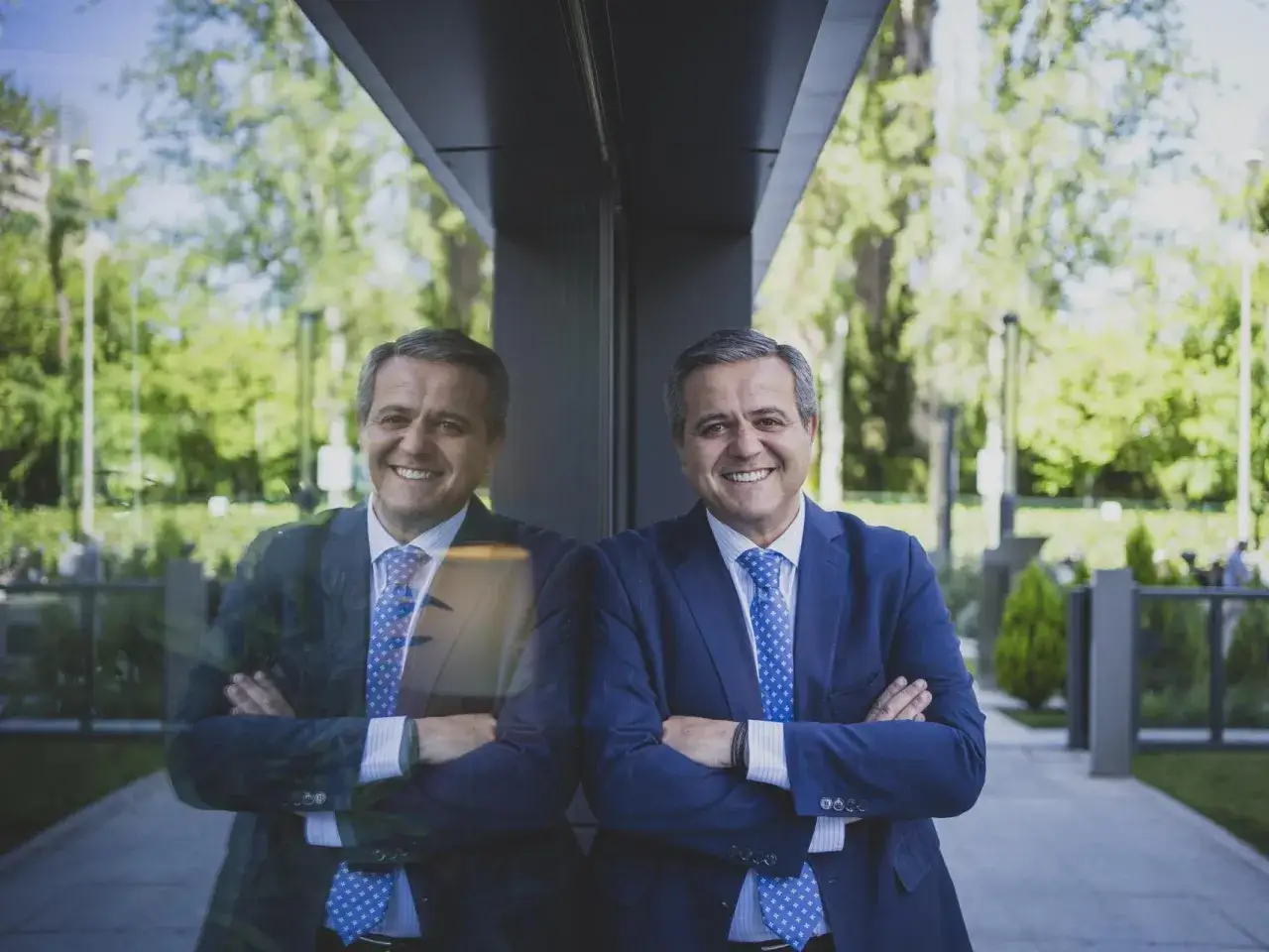 Hombre sonriente con traje azul, reflejado en un cristal. Parece un director de obras con experiencia, listo para supervisar el pr&oacute;ximo gran proyecto.