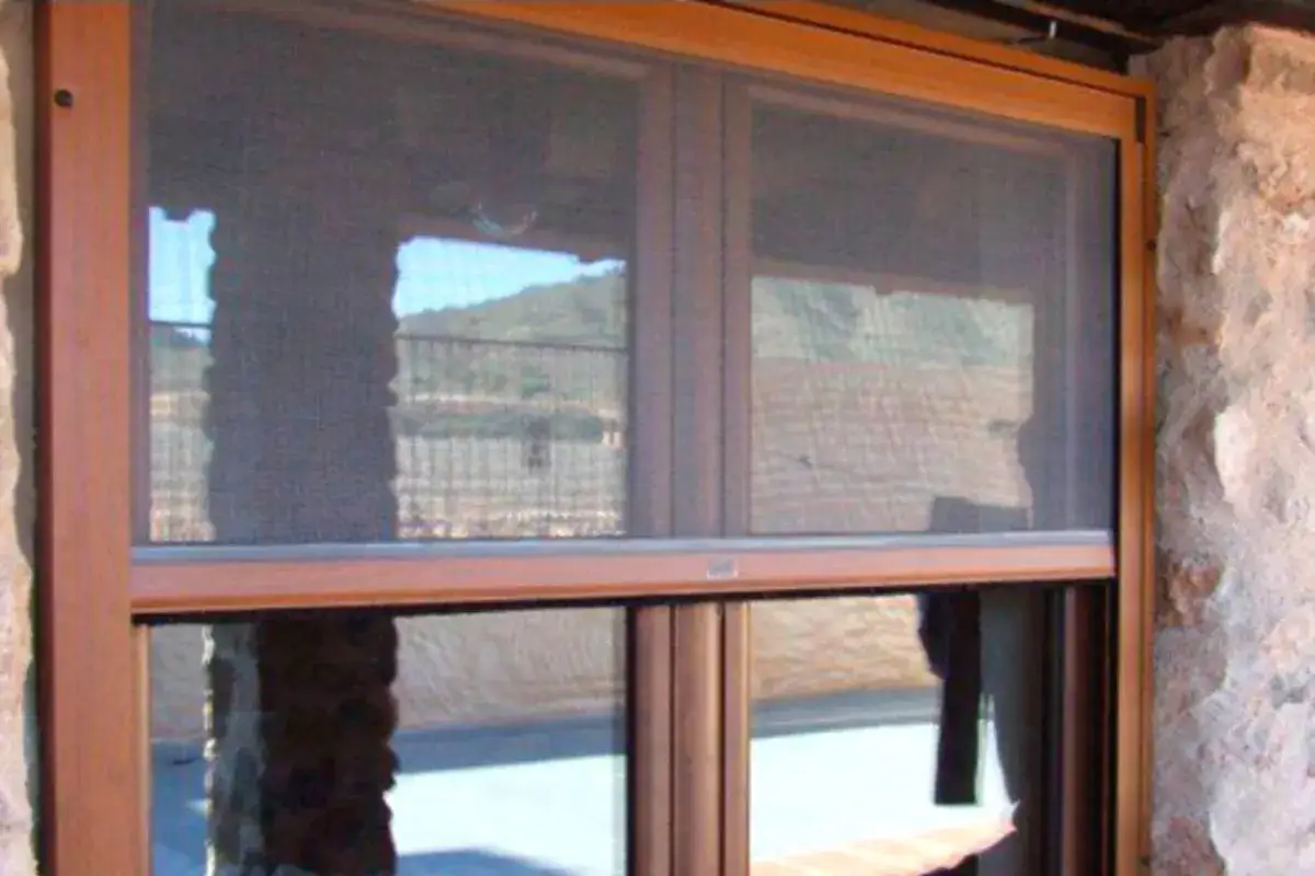 Instalaci&oacute;n de mosquiteras en ventana de madera con vistas a un paisaje monta&ntilde;oso. Protege tu hogar de insectos.