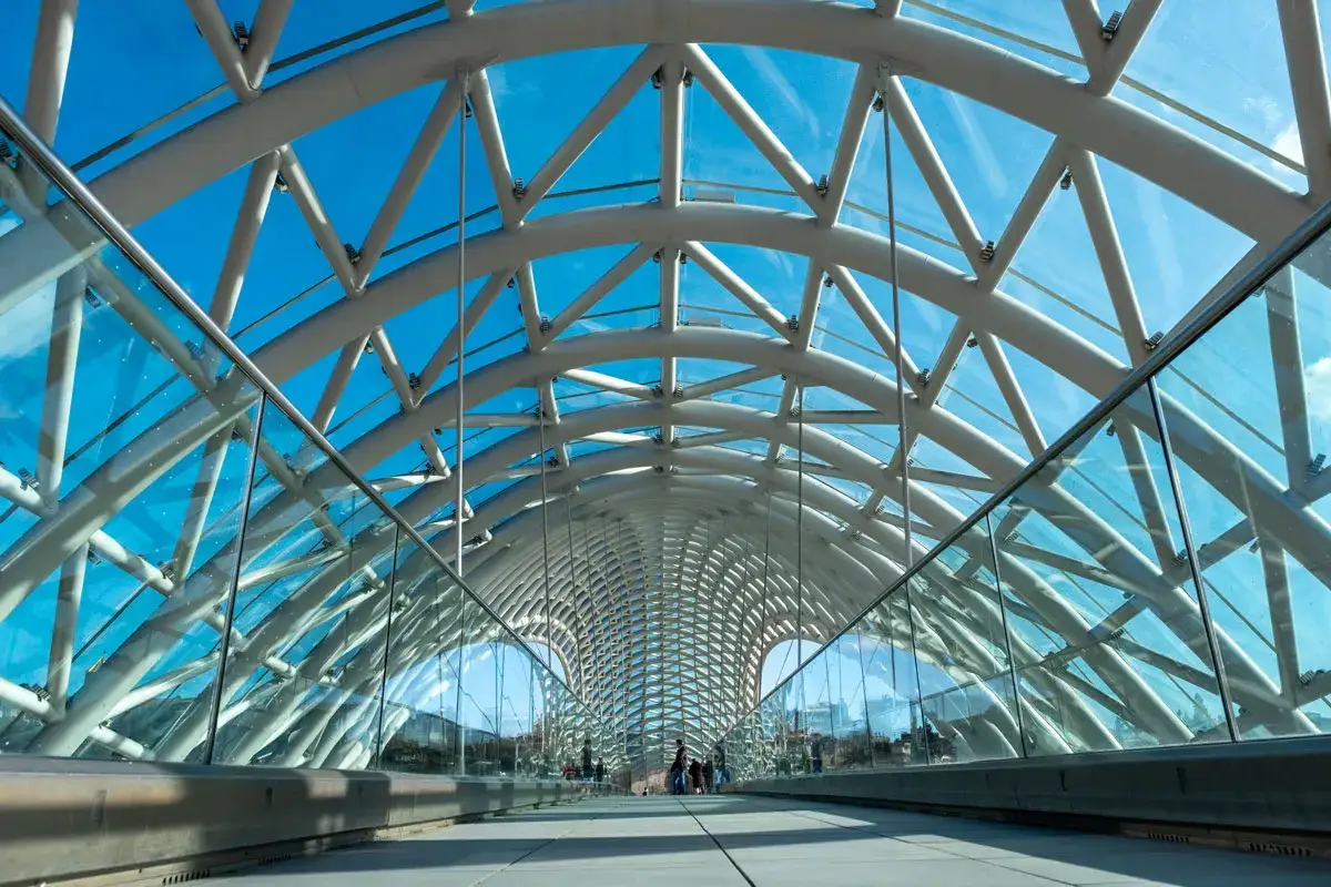 Pasarela moderna con techo de cristales curvos y estructura met&aacute;lica blanca contra un cielo azul brillante.