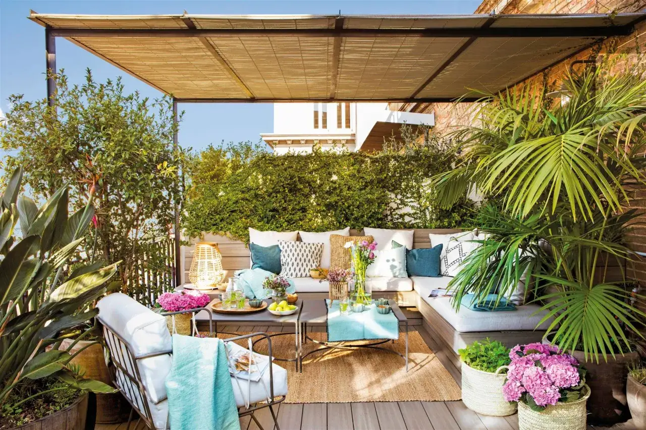 Elegante decoracion terrazas con sofá, mesas bajas, plantas exuberantes y cojines coloridos bajo un toldo de bambú.