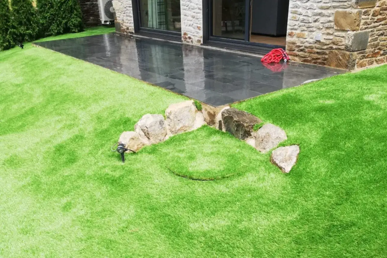 Instalaci&oacute;n de c&eacute;sped artificial con rocas y un foco de luz, creando un jard&iacute;n moderno y de bajo mantenimiento.
